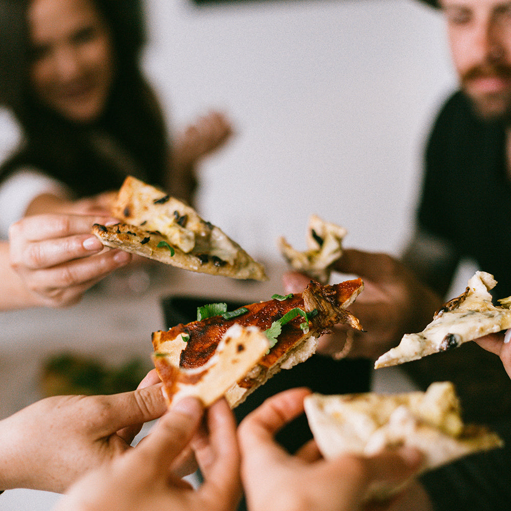 A photo of several people cheersing with slices of pizza.